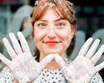 woman with smiling towards the camera with her hands facing forward creating a 'w' shape - her hands and hair have flour on them