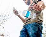 man looking at his phone while dropping an empty plastic bottle onto the ground