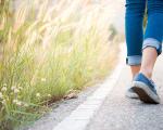 Legs of a woman wearing blue jeans and blue trainers walking up a road