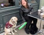 lady sat outside a café with her guide dog. She's smiling at the camera