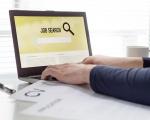 man sat at a white desk with laptop open on a job search screen