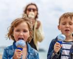 two children eating ice cream on a beach with their mother in the background