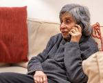 elderly lady wearing a grey sweatshirt and sitting on a sofa while talking on the phone