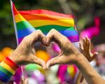 hands creating a heart symbol in front of rainbow pride flags