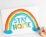 child's painting of a rainbow with the words Stay Home painted underneath