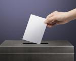 hand placing a piece of paper into a voting ballot box