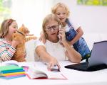 lady working at home on a laptop while talking on the phone and looking after her two small children