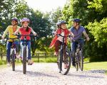 Family of four riding their bikes down a path with green trees behind them