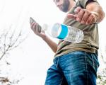 person looking at their phone while dropping an empty plastic bottle onto the ground