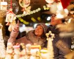 man and woman wearing winter clothes looking at items at a Christmas market stall covered in lights