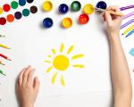 birds eye view of a child's arms over a piece of paper. The child is painting a yellow sunshine.