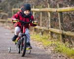small child wearing a grey woolly hat and a red coat riding a bike with stabilisers