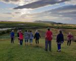 a group of people on sandy grass watching the sunset