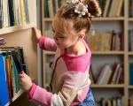 young girl with a magnifying glass inspecting books on a shelf