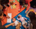 two babies laid on play mats with their parents say round them