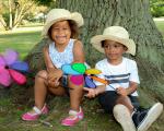 two children sat under a tree with summer hats on and windmills in their hands