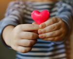 young child holding a small pink heart out in front of them