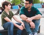 a boy and a young man sat on a bench talking