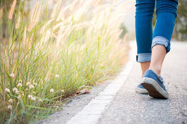 Legs of a woman wearing blue jeans and blue trainers walking up a road