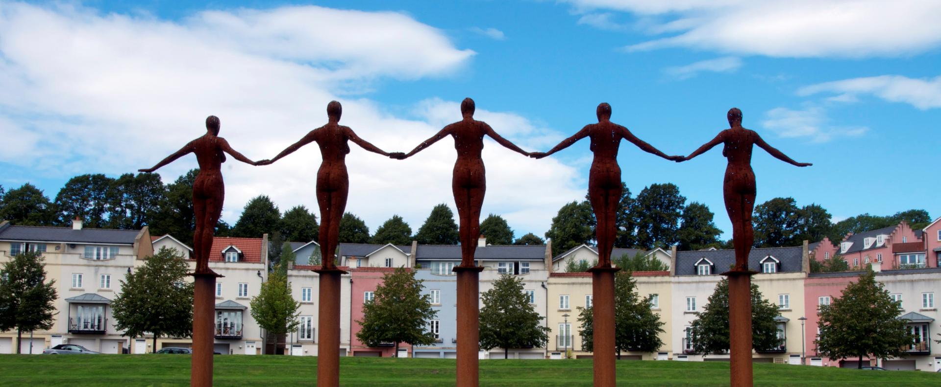 sculpture of five women standing together on pillars with their hands joined