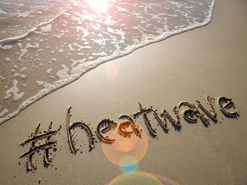 seawater lapping on a beach with the word' heatwave' written into the sand