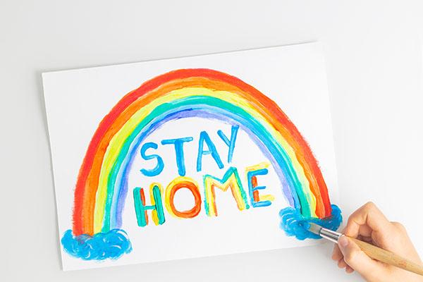 child's painting of a rainbow with the words Stay Home painted underneath