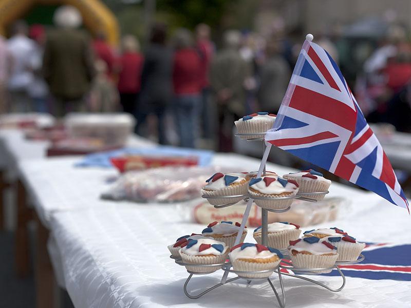 a long table set out for a street party. Table is covered by a white table cloth and on top are a selection of snacks and a Union Flag