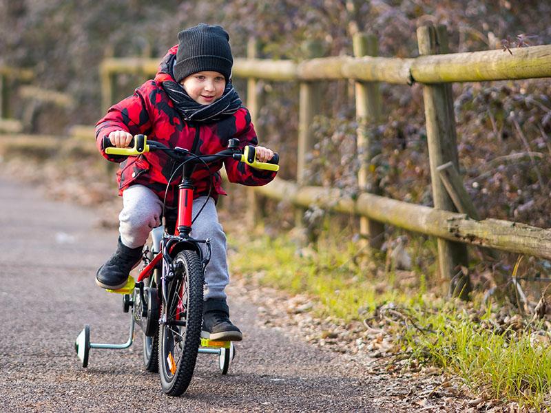 small child wearing a grey woolly hat and a red coat riding a bike with stabilisers 