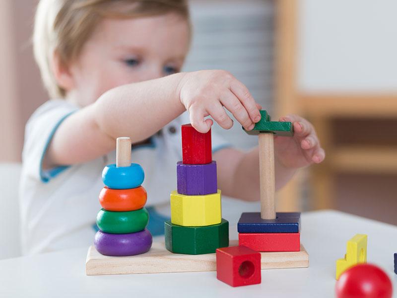 toddler stacking colour wooden blocks on a table