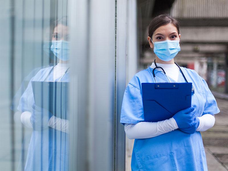 nurse in PPE holding a blue clipboard