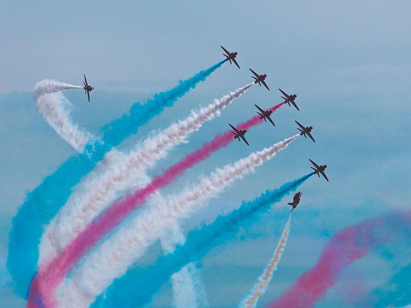 red arrows in the air with red, white and blue smoke trails behind them