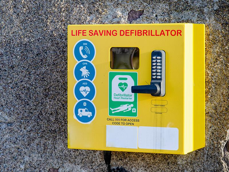 A yellow box defibrillator on a concrete wall