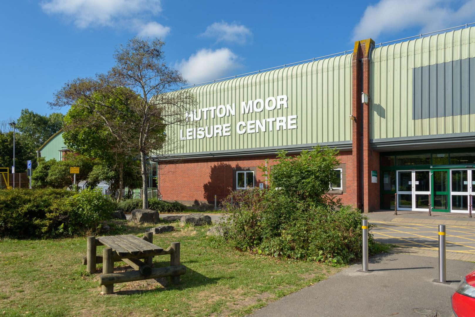 Hutton Moor Leisure Centre on a sunny day. A bench and trees are in front of the entrance