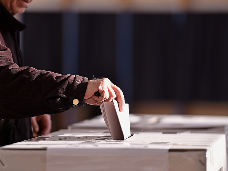 A hand putting a voting slip in a box