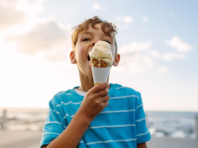 A boy licking an ice cream on a beach