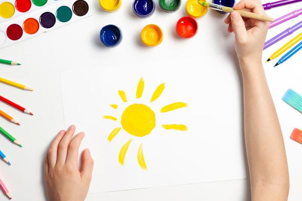 birds eye view of a child's arms over a piece of paper. The child is painting a yellow sunshine.