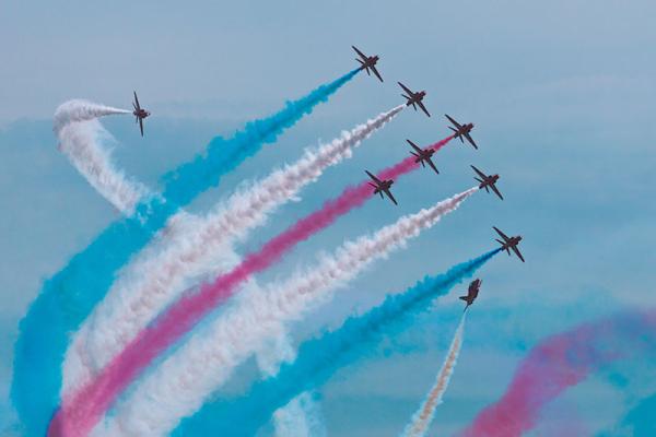 red arrows in the air with red, white and blue smoke trails behind them