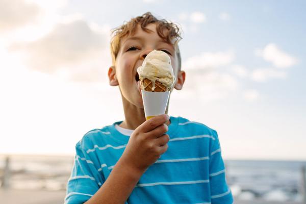 A boy licking an ice cream on a beach